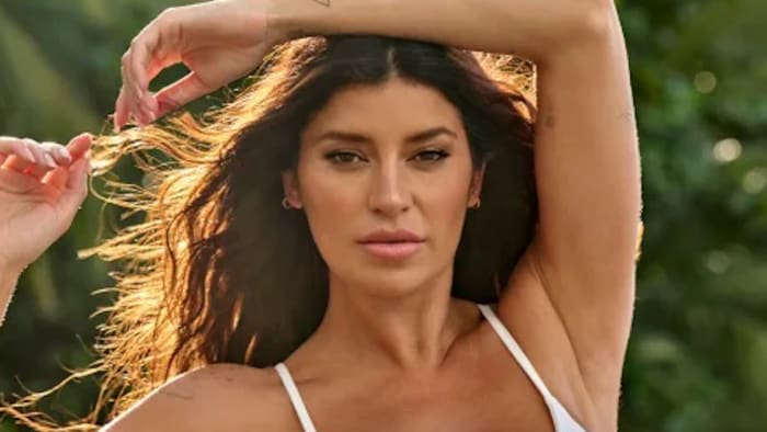 Nicole Williams English poses in a white bikini with her arm above her head.